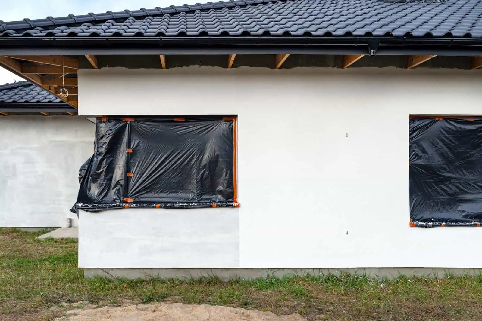 House exterior with fresh white paint and black window coverings under construction.