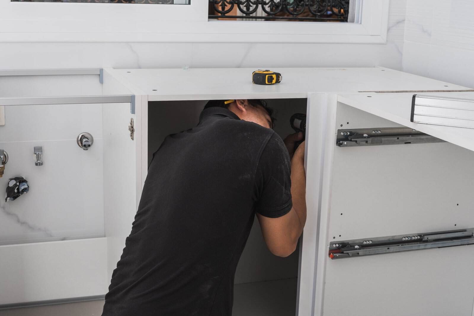 Professional installer working on kitchen cabinet assembly or repair.