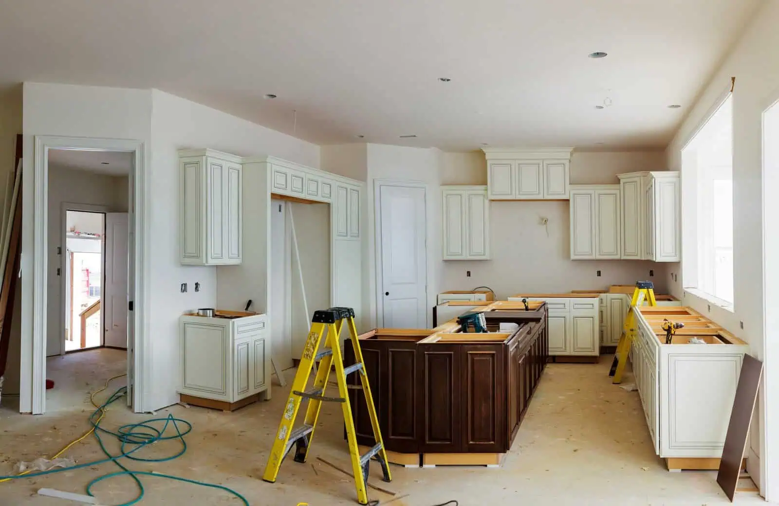 Kitchen under construction with white cabinets and yellow ladders.